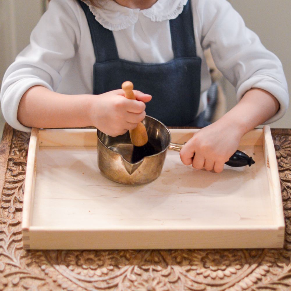 enfant qui utile une brosse à dépoussiérer avec un plateau d'activités Montessori pour nettoyer une petite casserole en argent