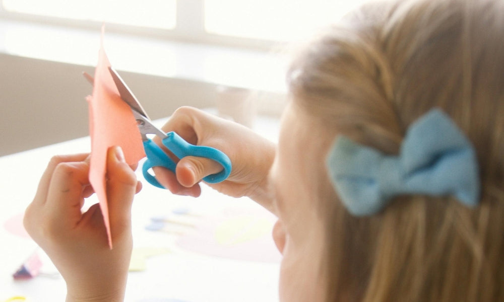 Une petite fille réalise une activité de découpage avec un ciseau bleu