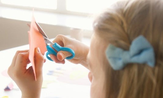 Une petite fille réalise une activité de découpage avec un ciseau bleu