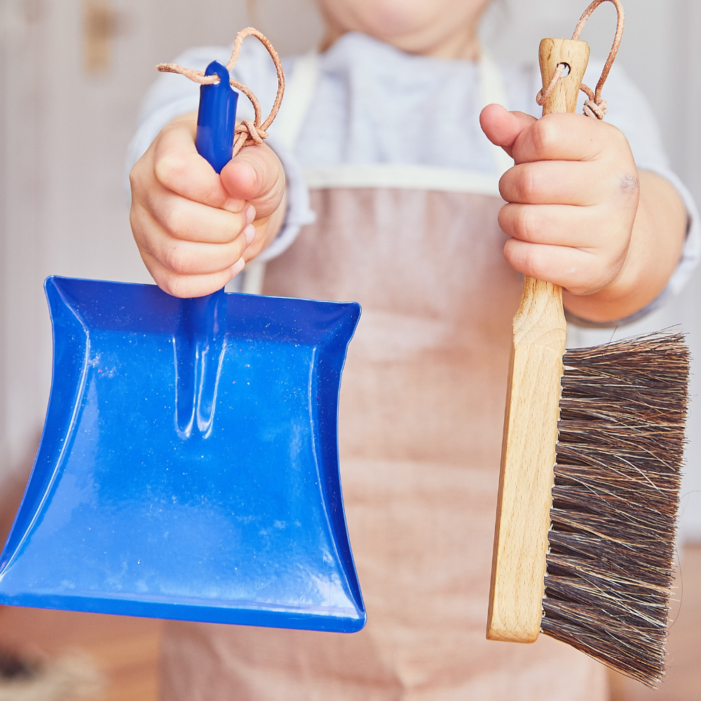 Petite fille présente une balayette et une pelle bleue taille enfant