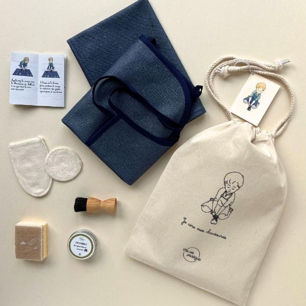 activité montessori de vie pratique : le kit enfant 3 ans, 4 ans ou 5 ans pour cirer ses chaussures tout seul, le kit contient un tablier déperlant enfant, un tapis d'activité montessori, un gant lavable pour cirer les chaussures, un coton d'application lavable, un cirage naturel, une borsse à lustrer pour enfant, une éponge enfant, un pochon sérigraphié et un tutotiel illustré pour présenter l'activité comme en école Montessori
